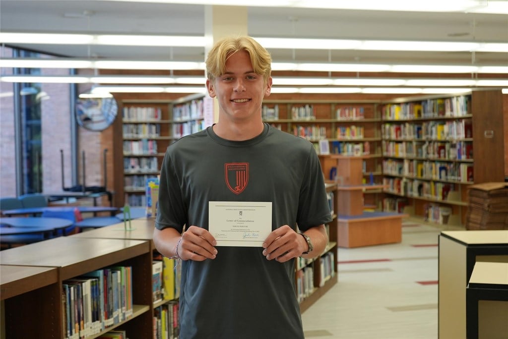 Sam Radulski stands with his certificate from the National Merit Scholarship Corporation.