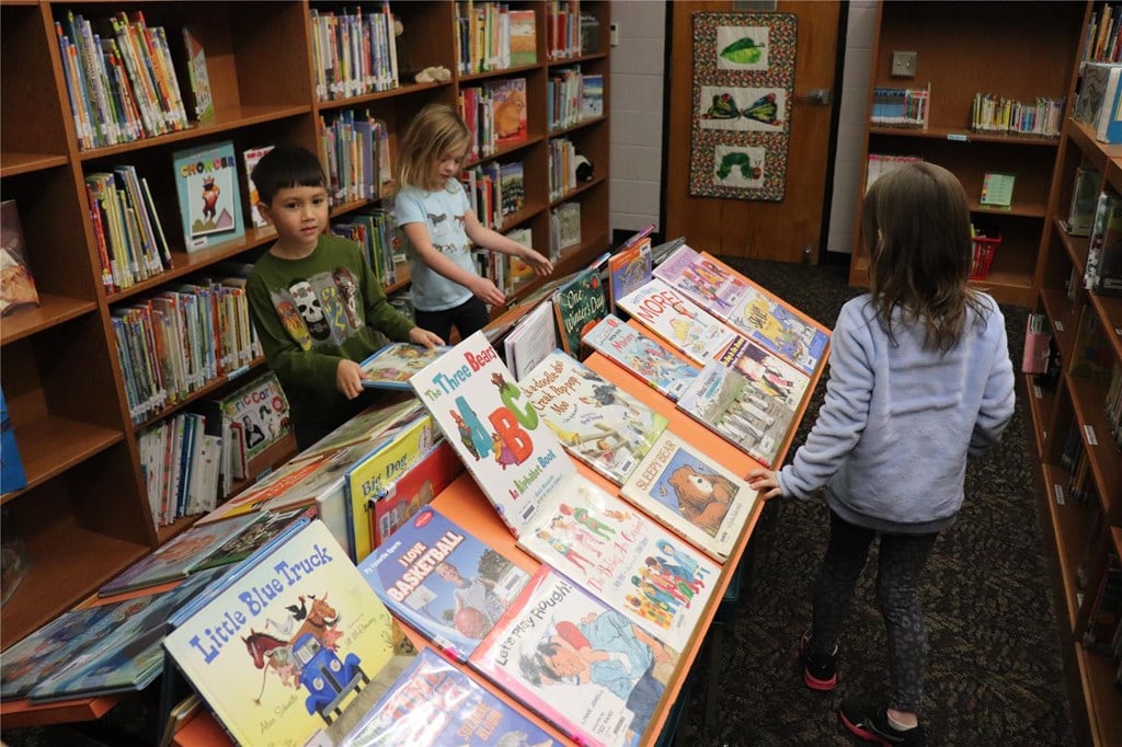 3 children looking at books in a library