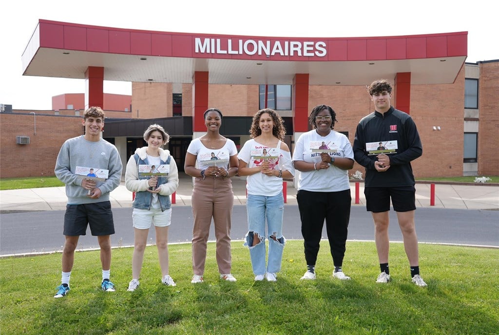 Students stand holding replicas of their billboards.