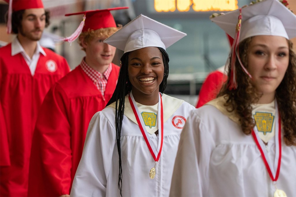 A student smiles at the camera during graduation procession