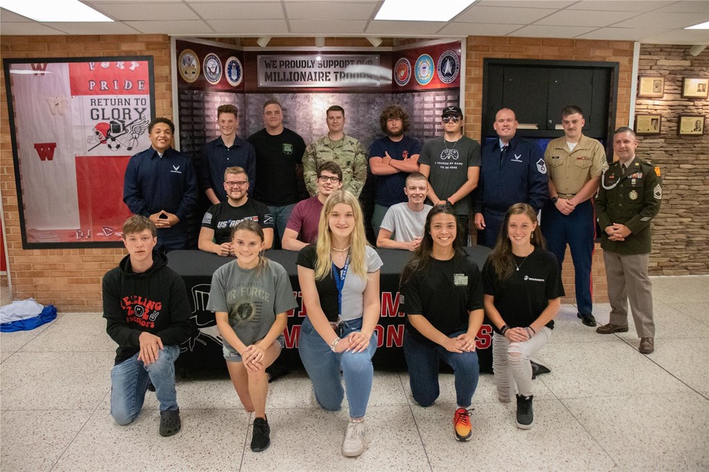 The 2022 military signees pose for a photo in front of the new Millionaire Military Wall.